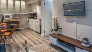Een moderne keuken met een magnetron, fornuis en kasten, een eethoek met stoelen en een tafel, en een tv aan de muur waarop een landschappelijk uitzicht te zien is.