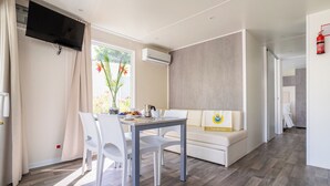A modern hotel room with a dining table, chairs, a sofa, a flat-screen TV, an air conditioning unit, and a fire extinguisher. - Club Del Sole Adriatico Cervia Easy Camping Village (Cervia)