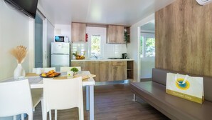 A modern kitchen with wooden cabinets, a refrigerator, and a dining area with a table and chairs. - Club Del Sole Adriatico Cervia Easy Camping Village (Cervia)