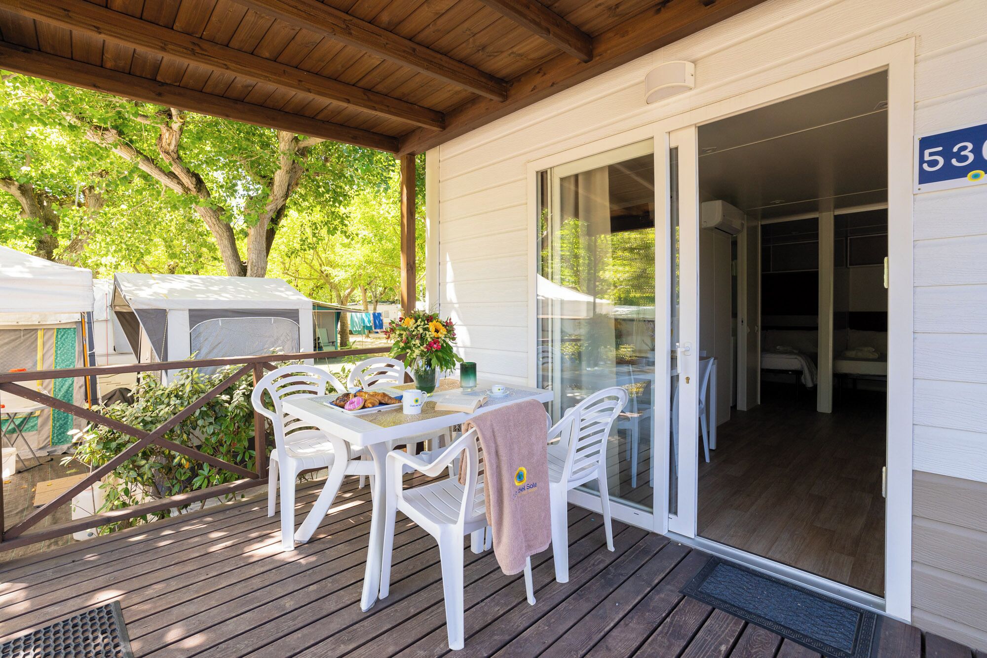 A covered outdoor seating area with a table and chairs, a window, and a door leading to a bedroom.