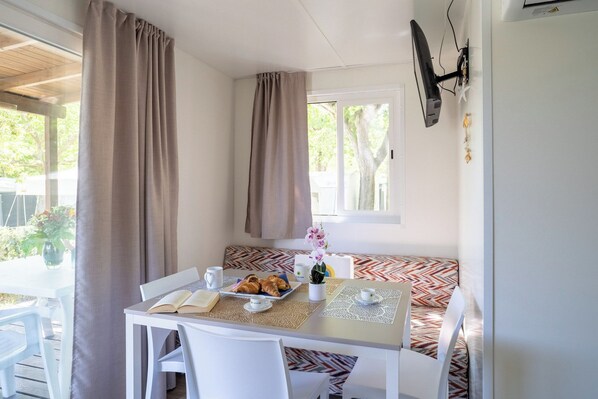 A room with a table set for breakfast, a bench, and a window with curtains. - Club Del Sole Adriatico Cervia Easy Camping Village (Cervia)
