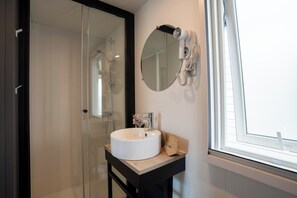 A bathroom with a glass shower enclosure, a white sink, a round mirror, and a hairdryer mounted on the wall. - Club Del Sole Adriatico Cervia Easy Camping Village (Cervia)