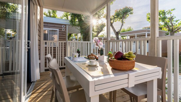 A covered outdoor dining area with a table, chairs, and a basket of fruit. - Club Del Sole Adriatico Cervia Easy Camping Village (Cervia)