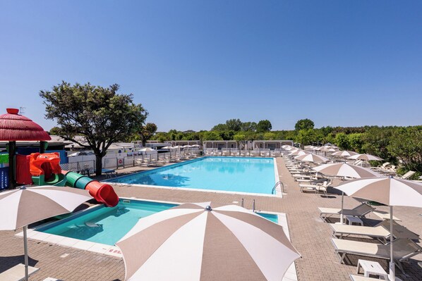A swimming pool with adjacent lounge chairs and umbrellas, a children's play area, and a clear sky. - Club Del Sole Adriatico Cervia Easy Camping Village (Cervia)