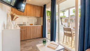 A modern kitchen with wooden cabinets, a flat-screen TV, and a dining area with a table and chairs. - Club Del Sole Adriatico Cervia Easy Camping Village (Cervia)