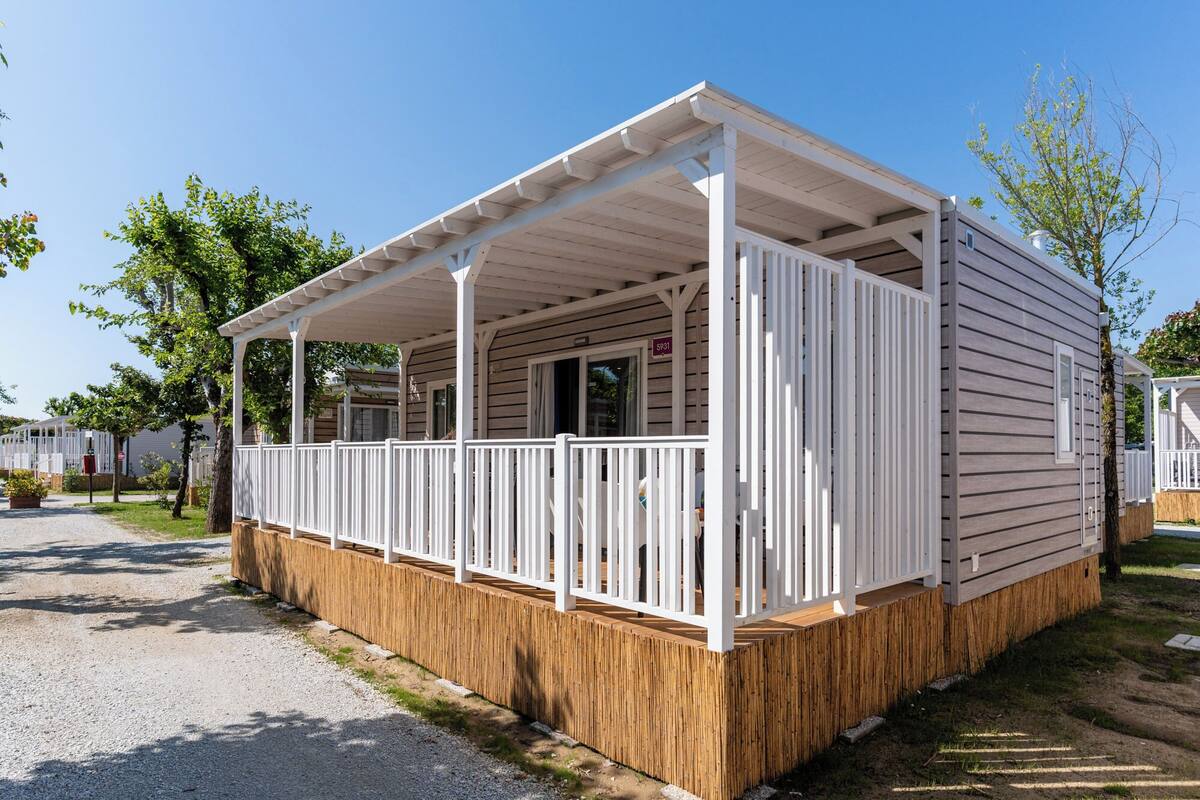 A single-story mobile home with a covered porch, wooden deck, and a fenced yard.