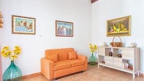 A room with a sofa, a cabinet with bowls, and two vases with flowers. - Apartment 'Nonna Rosa' with Private Terrace, Shared Garden and Air Conditioning (Pachino)