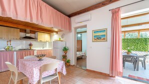 A kitchen with a dining area, a bed, and a view of the outdoors. - Apartment 'Nonna Rosa' with Private Terrace, Shared Garden and Air Conditioning (Pachino)