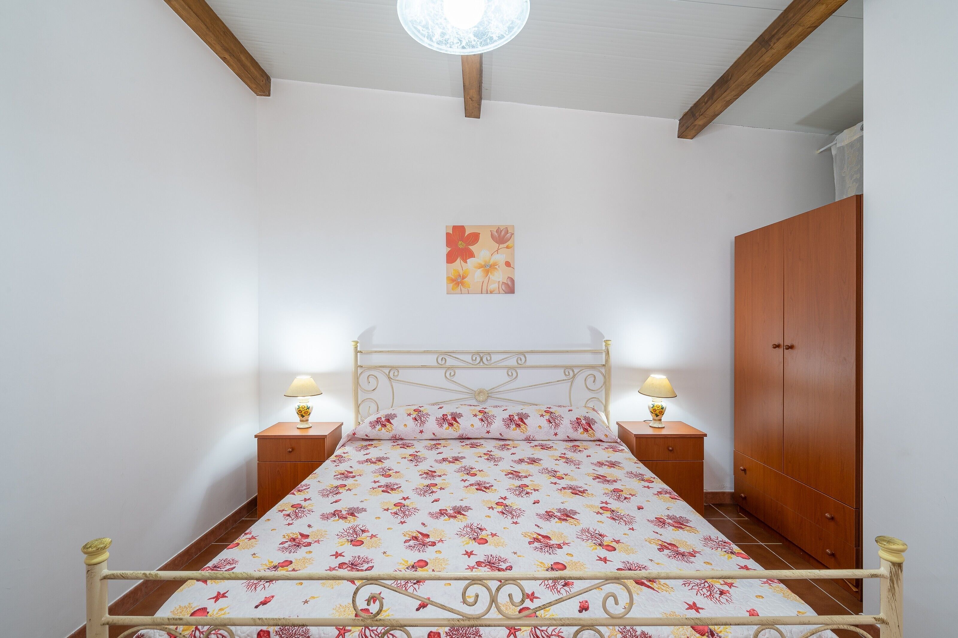 A bedroom with a bed, bedside lamps, a wooden wardrobe, and a wall-mounted artwork.