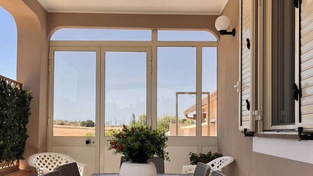 A sunlit patio with a table and chairs, a potted plant, and a view of the landscape. - Apartment 'Nonna Rosa' with Private Terrace, Shared Garden and Air Conditioning (Pachino)