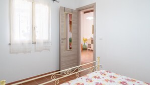 A bedroom with a bed, a wooden door, and a window with sheer curtains. - Apartment 'Nonna Rosa' with Private Terrace, Shared Garden and Air Conditioning (Pachino)