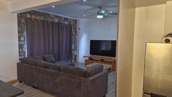 A living room with a sofa, a flat-screen TV, a wooden entertainment unit, and a stone wall.