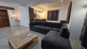 A modern living room with a sectional sofa, a wooden coffee table, and a dining area visible through an open doorway.