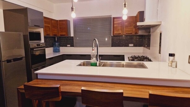 A modern kitchen with a central island, stainless steel appliances, wooden cabinets, and pendant lighting.