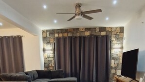 A living room with a sectional sofa, a coffee table, a TV stand, and a ceiling fan.