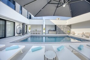 Un espace piscine extérieur moderne, doté de chaises longues et de parasols.