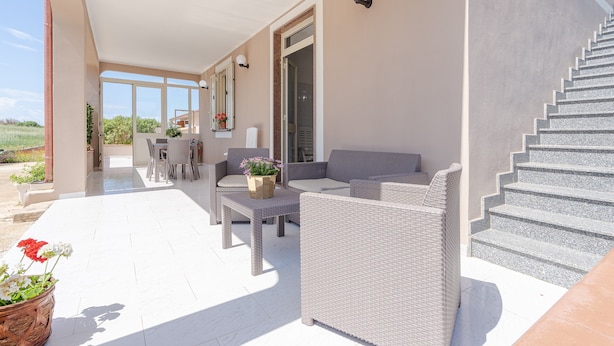 A covered outdoor area with wicker furniture, a staircase, and a view of the landscape. - Villa 'Con Tre Camere Da Letto' with Private Terrace, Shared Garden and Air Conditioning (Pachino)