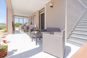 A covered outdoor area with wicker furniture, a staircase, and a view of the landscape. - Villa 'Con Tre Camere Da Letto' with Private Terrace, Shared Garden and Air Conditioning (Pachino)