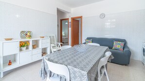 A compact living space with a dining table, a sofa, a washing machine, and a clock on the wall. - Villa 'Con Tre Camere Da Letto' with Private Terrace, Shared Garden and Air Conditioning (Pachino)