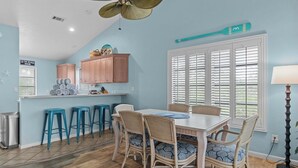 A kitchen with a dining area, wooden cabinets, a ceiling fan, and a window with blinds.