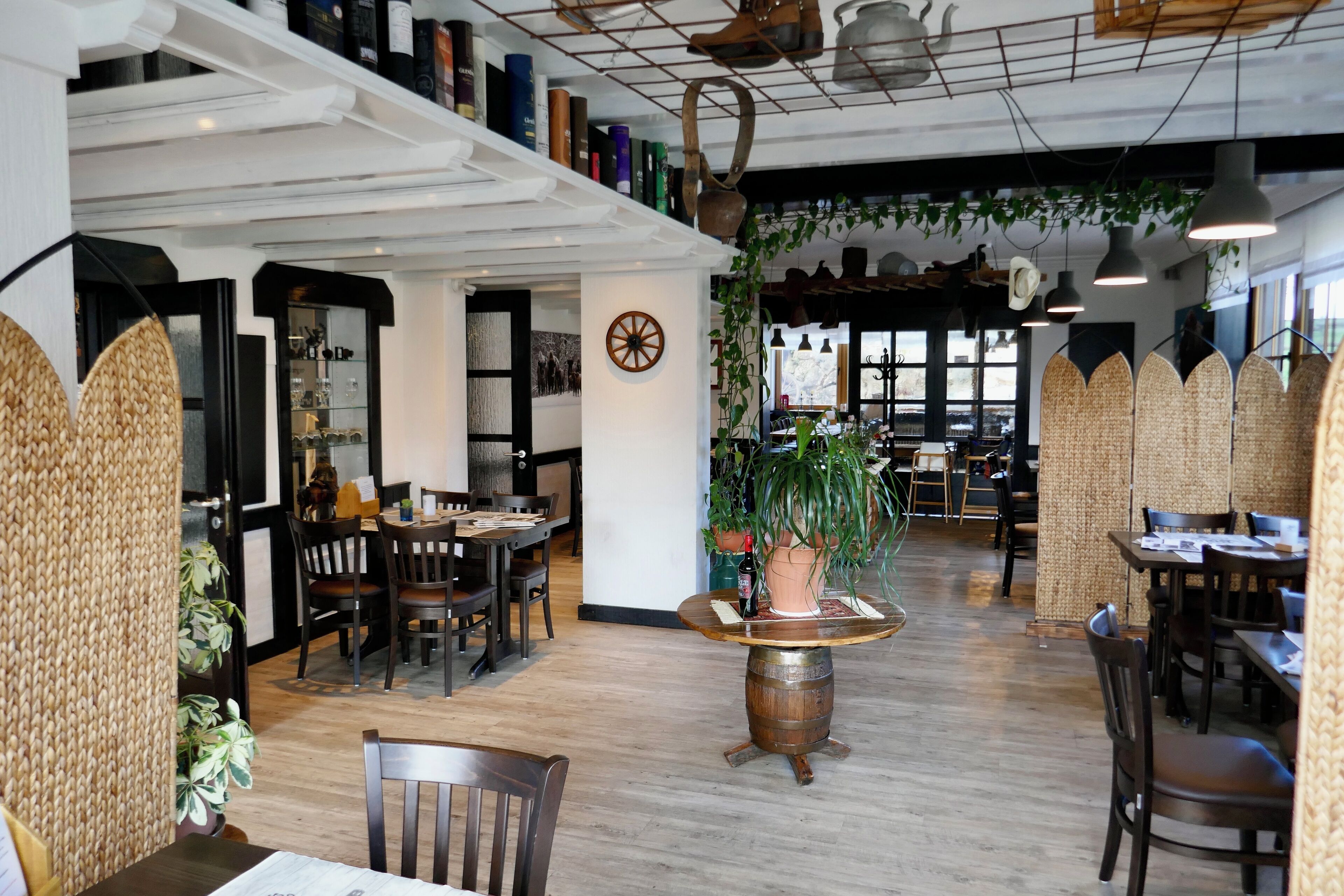 A restaurant interior with wooden tables, chairs, hanging plants, and a rustic wooden barrel as a centerpiece.