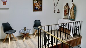 A room with a wooden floor, two black chairs, a small table with a checkered tablecloth, a wooden bench, and a railing.
