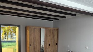A bedroom with a wooden bed, a wardrobe, and a view of a tropical landscape.