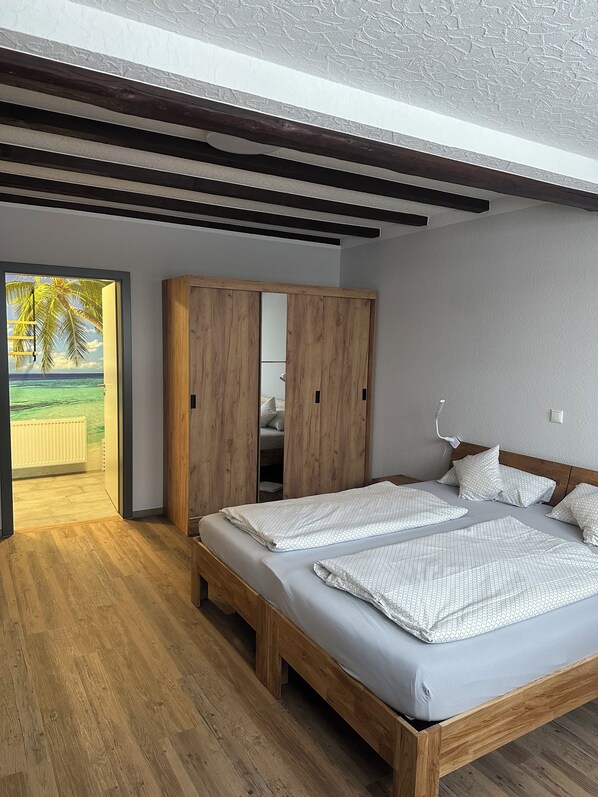 A bedroom with a wooden bed, a wardrobe, and a view of a tropical landscape.