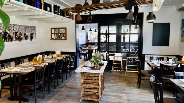 A restaurant with wooden tables and chairs, a central island, and a view through large windows.