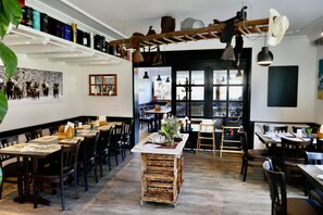 A restaurant with wooden tables and chairs, a central island, and a view through large windows.