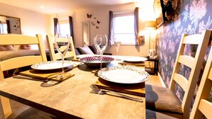 A dining area with a table set for two, featuring a floral wallpaper, a mirror, and a window with curtains. - 7 Domus House Studio Apartment -  a studio that sleeps 2 guests  in 1 bedroom (Chester)