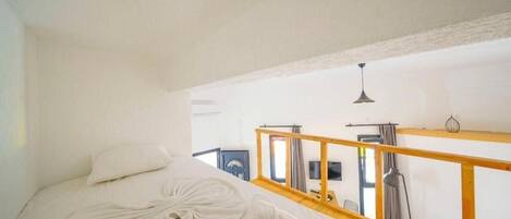 A bedroom with a bed, a wooden headboard, a window with curtains, and a hanging light fixture.
