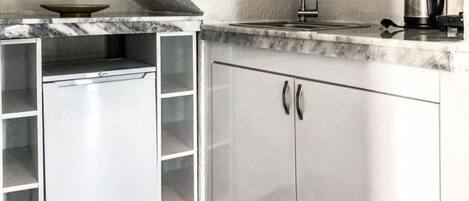 Une cuisine compacte équipée d’un lave-vaisselle intégré, d’un évier et d’une bouilloire.