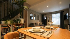 A dining area with a wooden table set for two, surrounded by bookshelves and a staircase. - The Cozy Nook -  an annex that sleeps 2 guests  in 1 bedroom (Chester)
