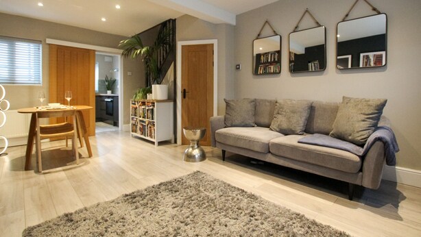 A modern living room with a grey sofa, a wooden dining table, and a large mirror on the wall. - The Cozy Nook -  an annex that sleeps 2 guests  in 1 bedroom (Chester)