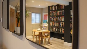 A room with a dining table, chairs, a bookshelf, and a mirror reflecting the room. - The Cozy Nook -  an annex that sleeps 2 guests  in 1 bedroom (Chester)