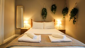 A hotel room with a large bed, two bedside tables with lamps, a mirror, and hanging plants. - The Cozy Nook -  an annex that sleeps 2 guests  in 1 bedroom (Chester)