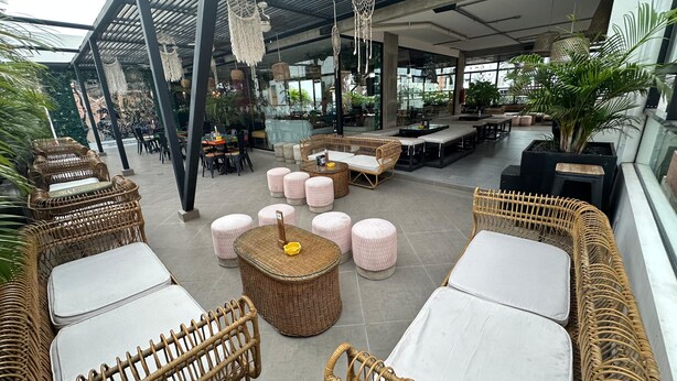 A spacious indoor area with wicker furniture, round tables, and a high ceiling with hanging dreamcatchers.