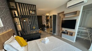 A modern hotel room with a large bed, a TV, a desk, and a seating area.