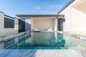 A swimming pool with a glass top, adjacent to a white building with a tiled roof. - House with private pool, Wi-Fi and air conditioning (Saint-Géniès-de-Malgoirès)