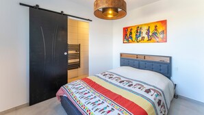Un dormitorio con cama, puerta corredera, un cuadro y una lámpara colgante.