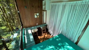 A room with a bed, a desk, and a window overlooking a forest.
