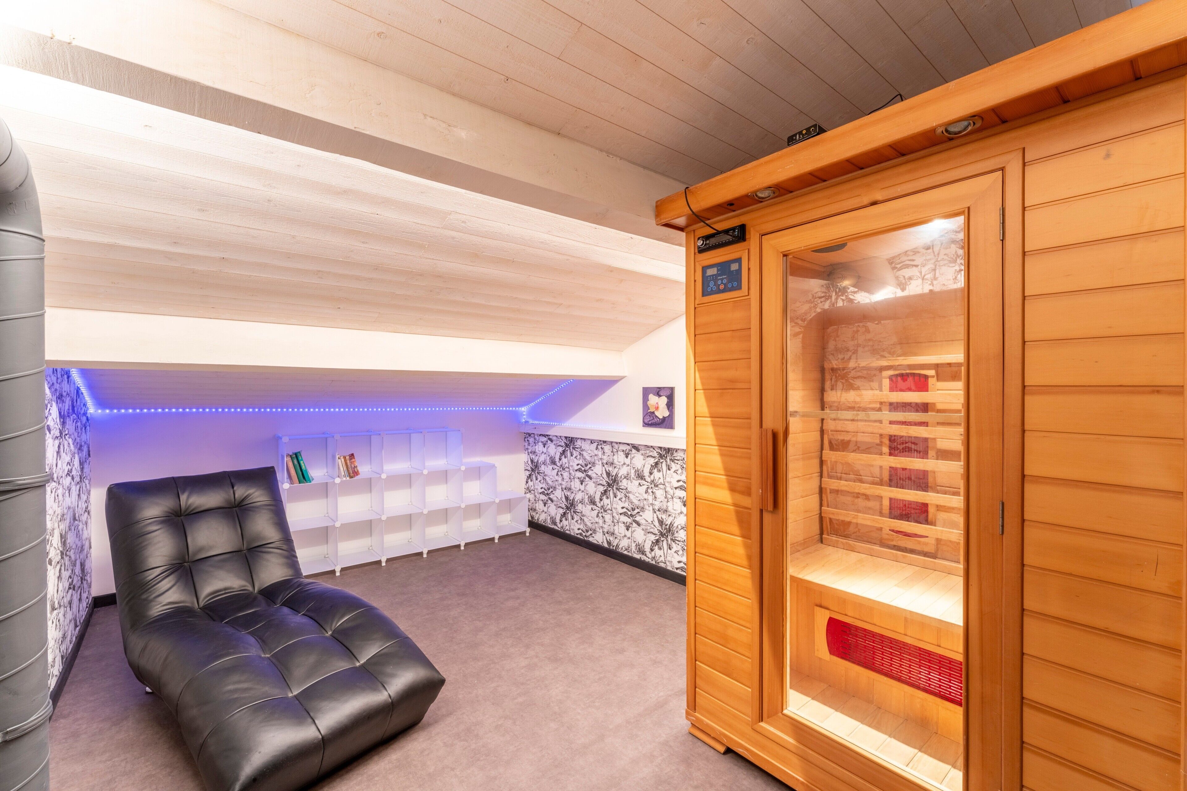 Un sauna avec un coffre en bois, un fauteuil de massage noir et une étagère blanche.