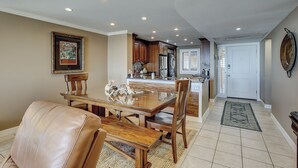 A dining area with a wooden table and chairs, a kitchen with modern appliances, and a hallway leading to a door. - Sunset Rentals | Island Club 5502 (Hilton Head Island)