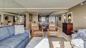 A spacious living room with a large sofa, two leather chairs, a coffee table, and a dining area with a kitchen in the background. - Sunset Rentals | Island Club 5502 (Hilton Head Island)