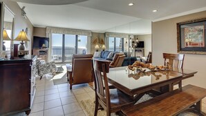 A spacious living room with a large window, a dining area with a wooden table, and a balcony with a view. - Sunset Rentals | Island Club 5502 (Hilton Head Island)