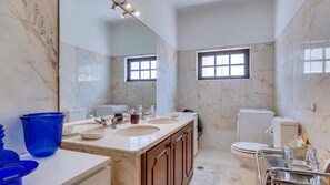 Ein Badezimmer mit Marmorwand, einem Doppelwaschtisch, einer Toilette und einem Fenster.