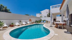 Ein Swimmingpool mit Liegestühlen und einem Tisch, umgeben von einem weißen Gebäude mit einem Kachel­dach.