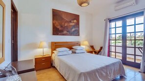 Ein Schlafzimmer mit einem Bett, zwei Nachttischen, einem Gemälde und einem großen Fenster.
