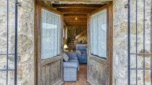 A narrow stone corridor with a wooden staircase leading to a room with a sofa and a lamp.